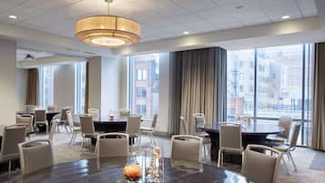 A modern conference room with round tables, comfortable chairs, and large windows offering city views.