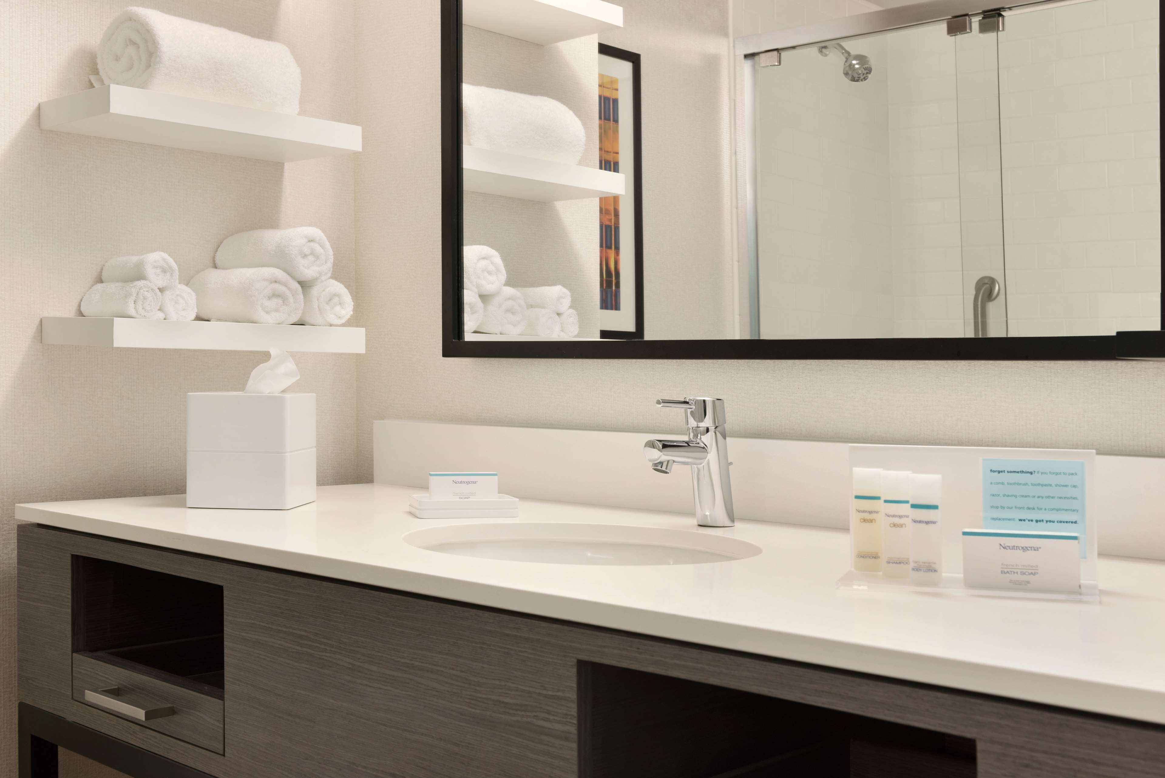 A modern bathroom with a white sink, a mirror, and shelves holding rolled towels.