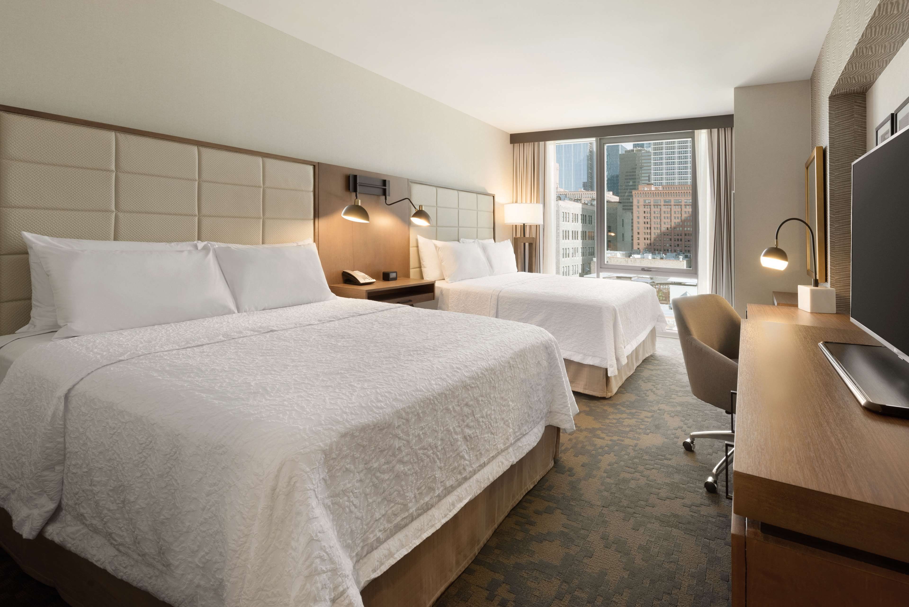 A hotel room with two beds, a desk, a chair, and a TV.