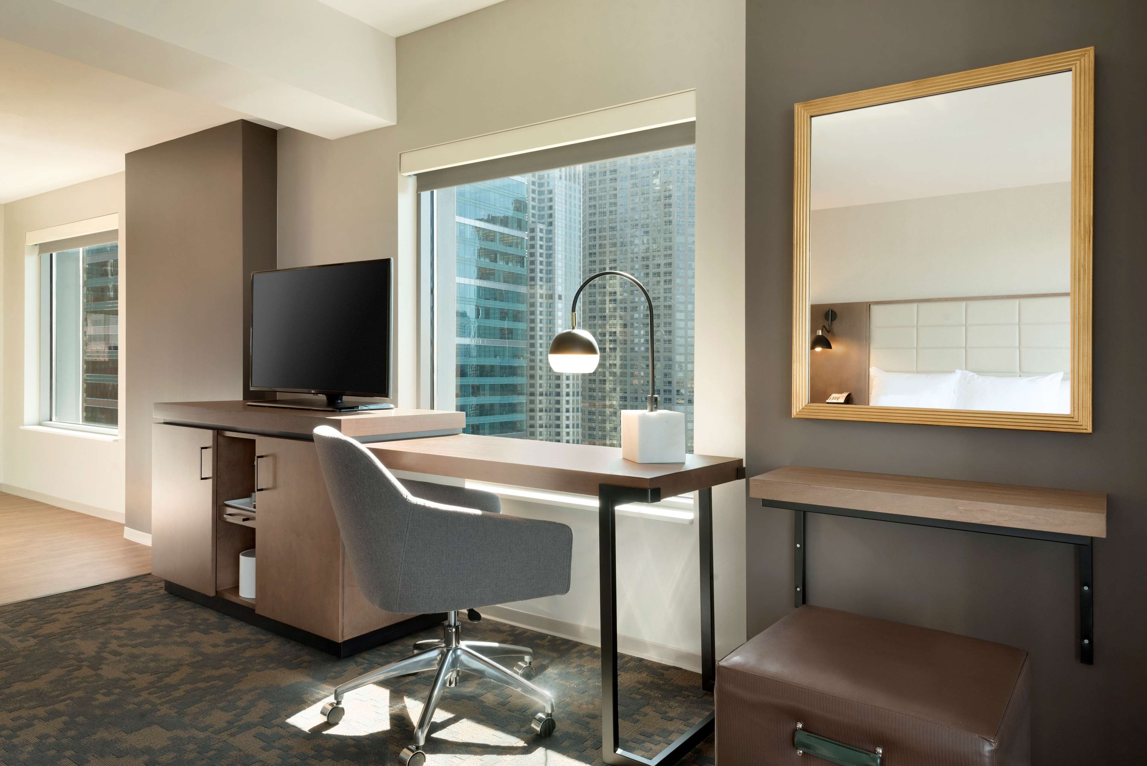 A modern hotel room with a desk, chair, television, and a large window with a city view.