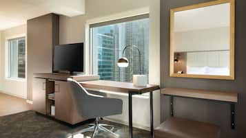 A modern hotel room with a desk, chair, television, and a large window with a city view.