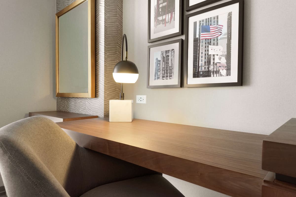 A modern desk with a lamp, framed pictures on the wall, and a mirror.