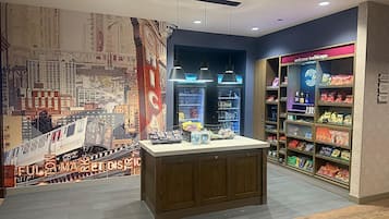 A modern retail space with a central wooden counter, a cityscape mural, and shelves stocked with snacks and beverages.