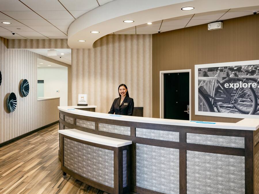 A hotel reception desk with a modern design, a receptionist, and a framed picture on the wall.