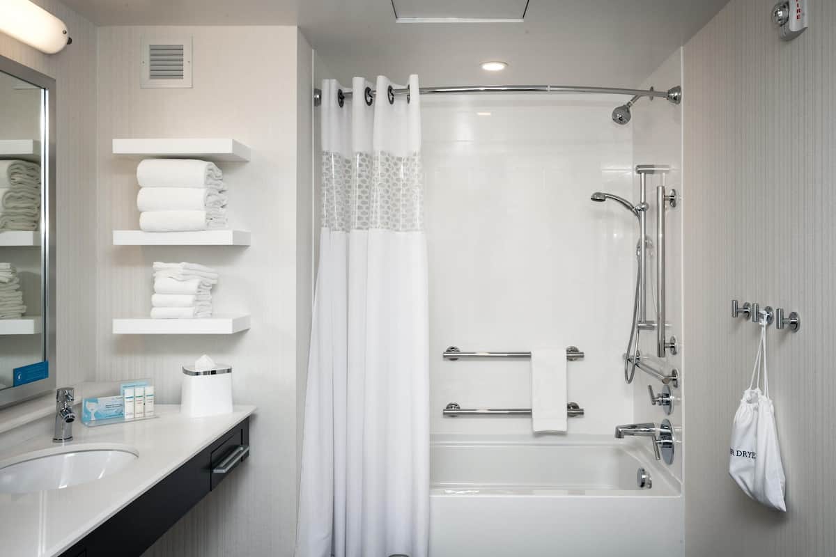 A modern bathroom with a bathtub, shower, and a vanity with a mirror and towel racks.