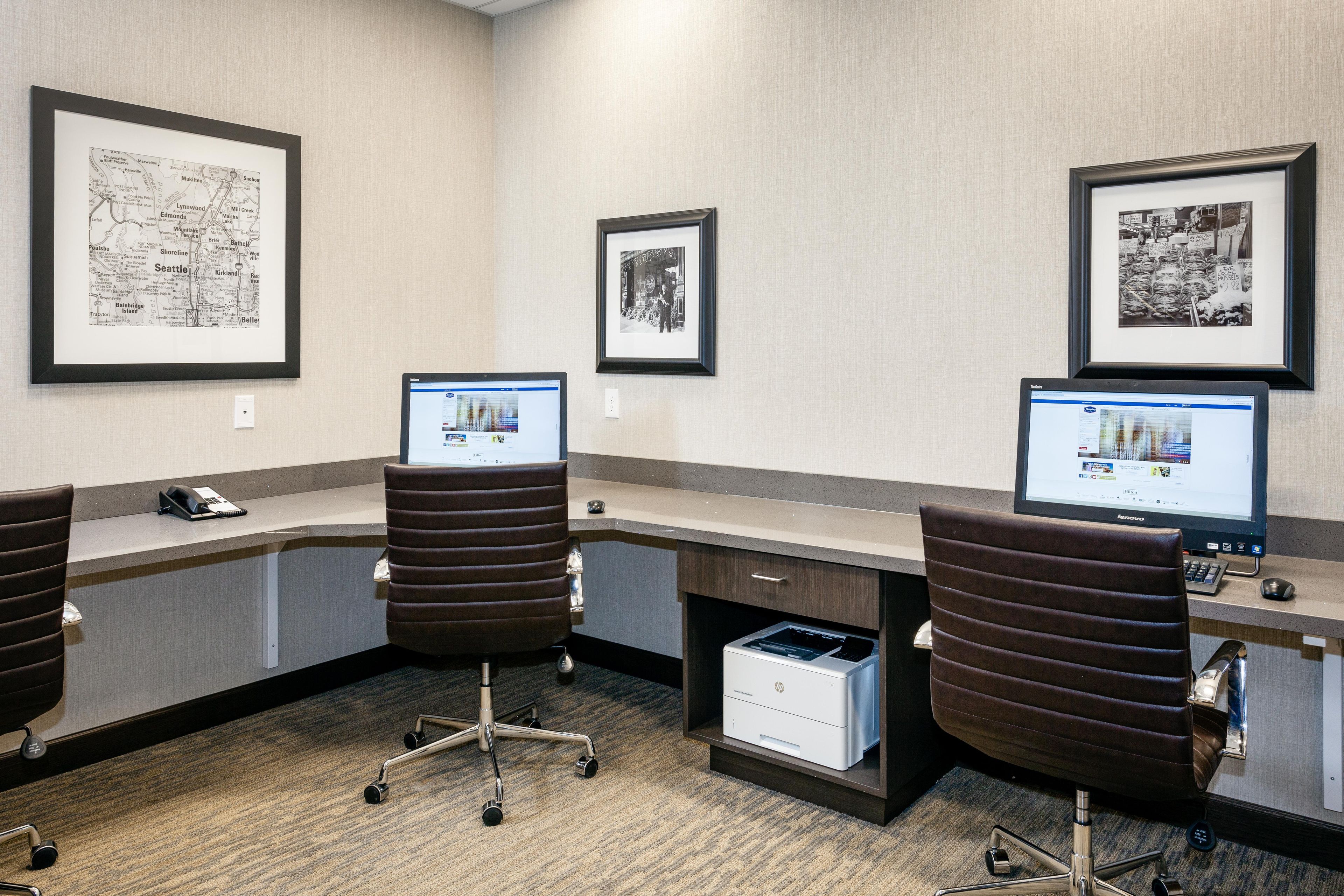 A hotel office with two desks, chairs, computers, and framed maps.