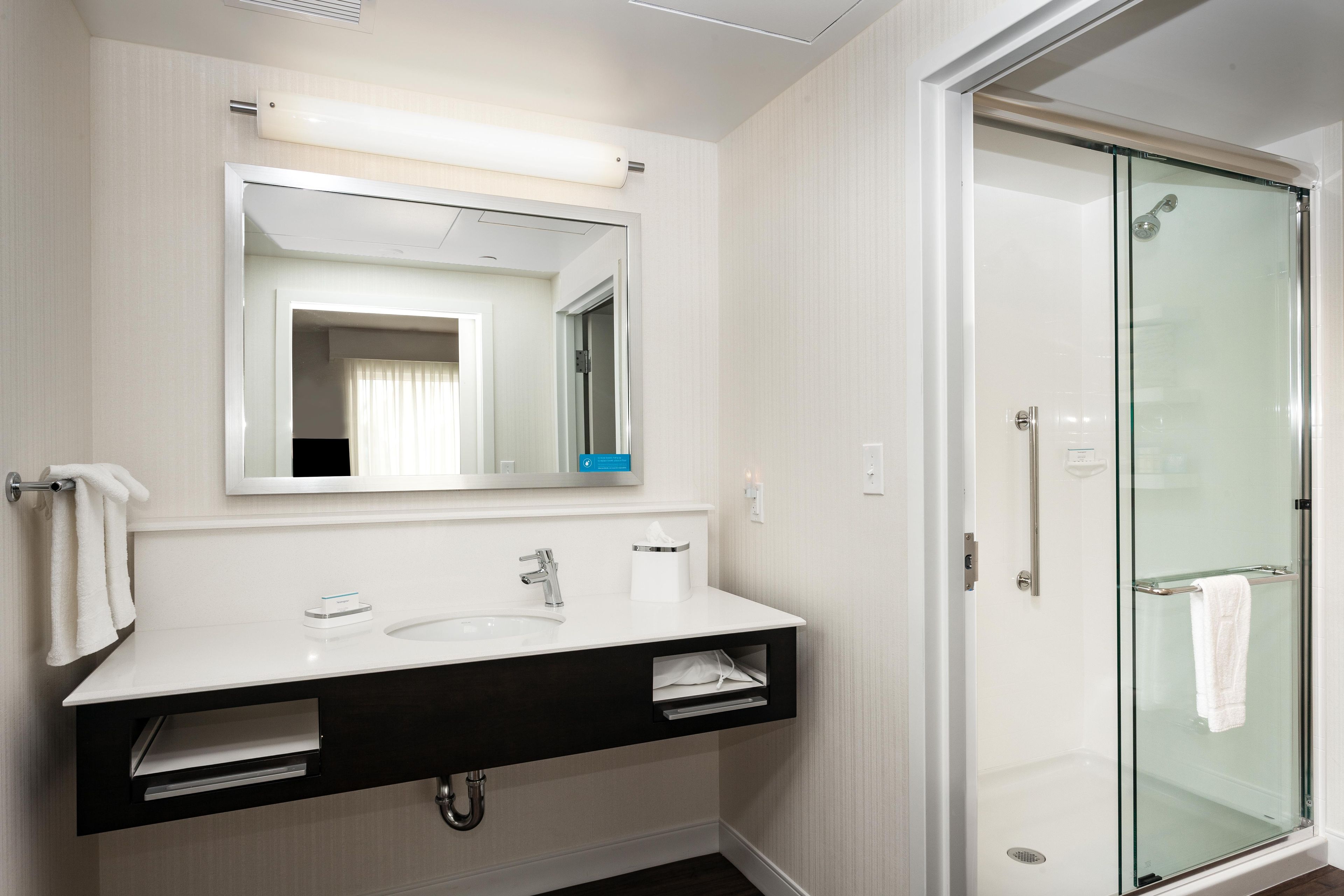 Een moderne badkamer met een glazen douchecabine, een witte wastafel met een zwart aanrecht en een spiegel erboven.