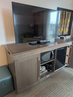 Quarto de hotel com televisão de tela plana presa a um armário, micro-ondas e pequena geladeira.