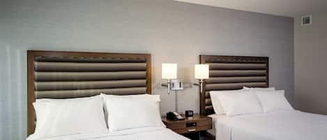 A hotel room with two beds, a nightstand with a lamp, and a telephone.