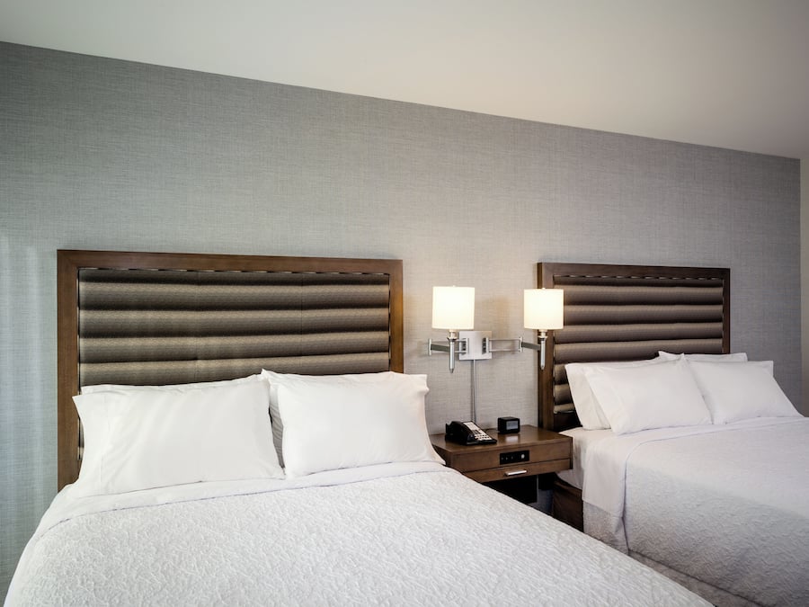 A hotel room with two beds, a nightstand with a lamp, and a telephone.