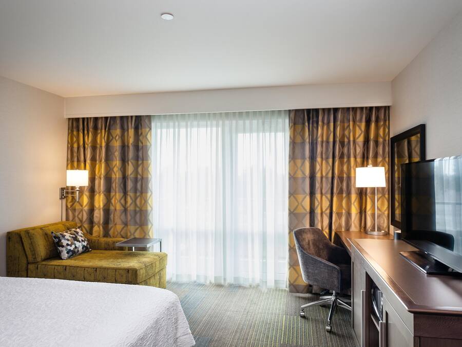 A hotel room with a bed, a desk with a television, a chair, a sofa, and curtains.