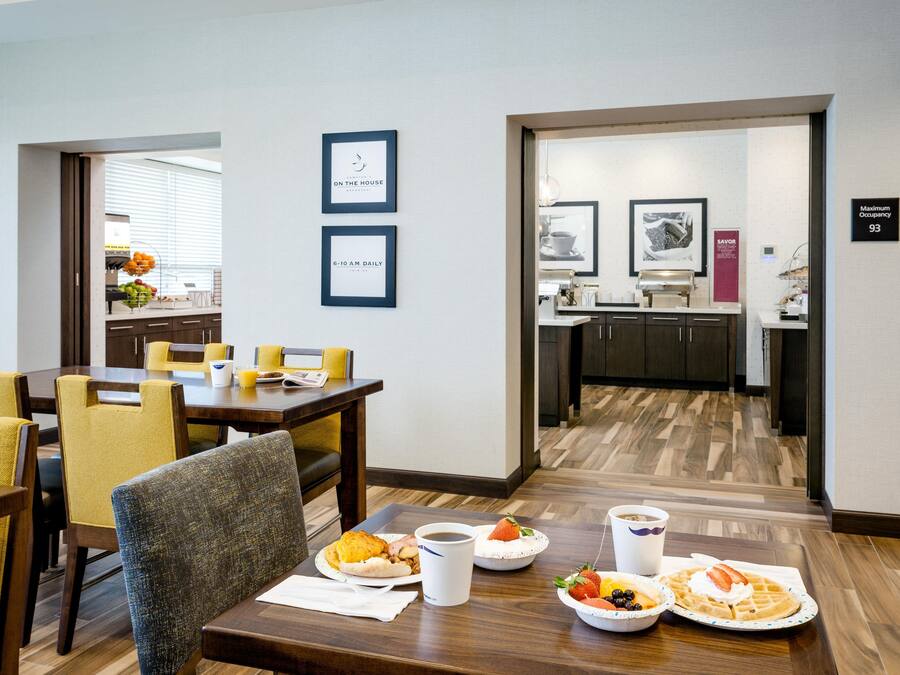A dining area with a breakfast setting including plates of food, a coffee cup, and a sign indicating 'Maximum Occupancy 93'.