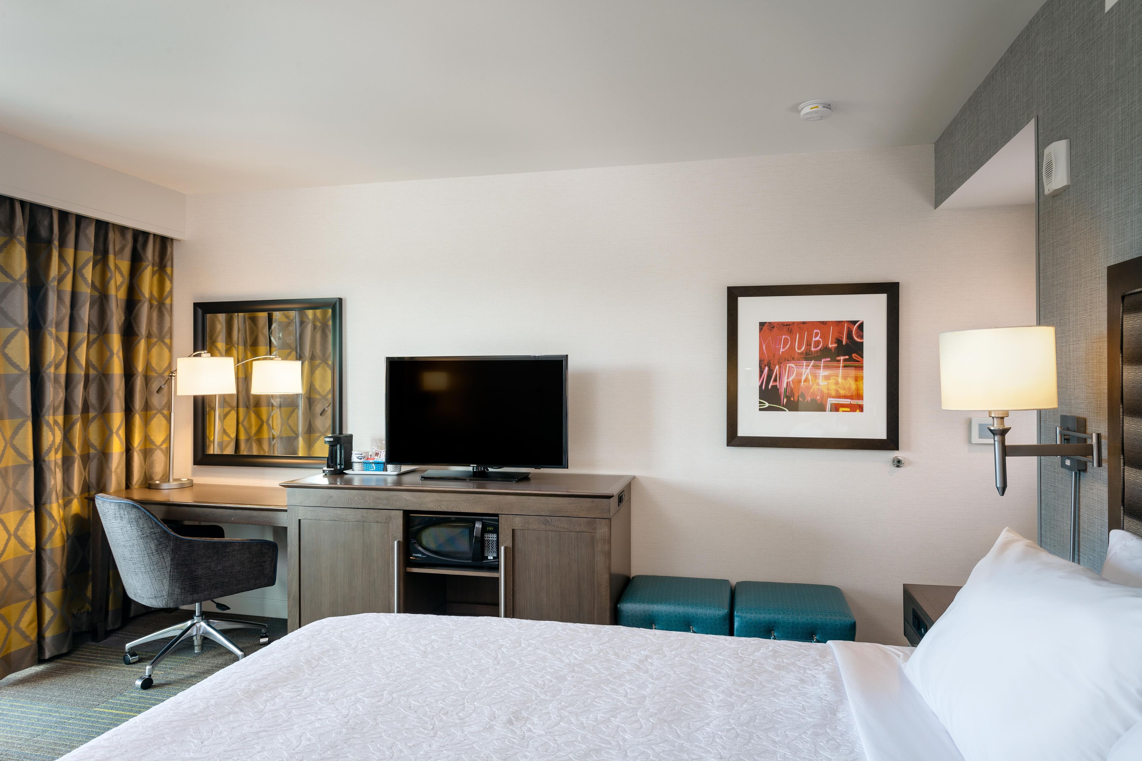 Una habitación de hotel con cama, escritorio, televisor y obras de arte en las paredes.