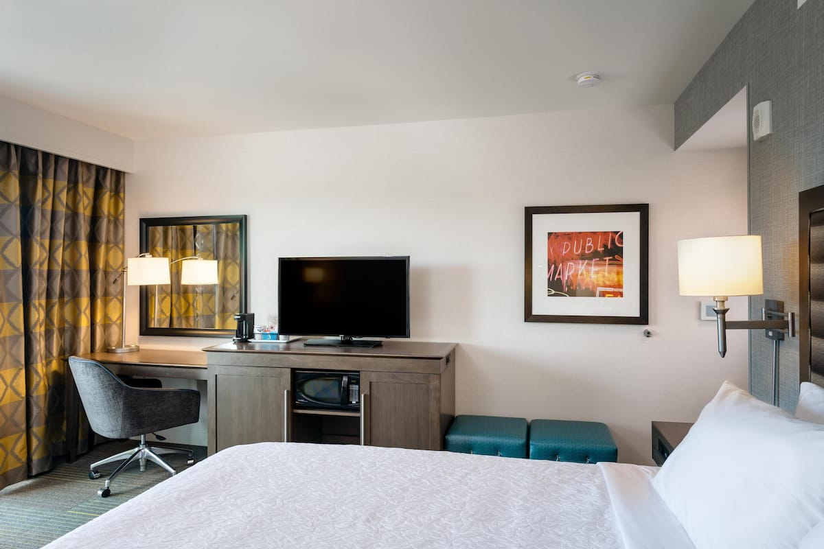 A hotel room with a bed, desk, chair, television, and two wall-mounted lamps.