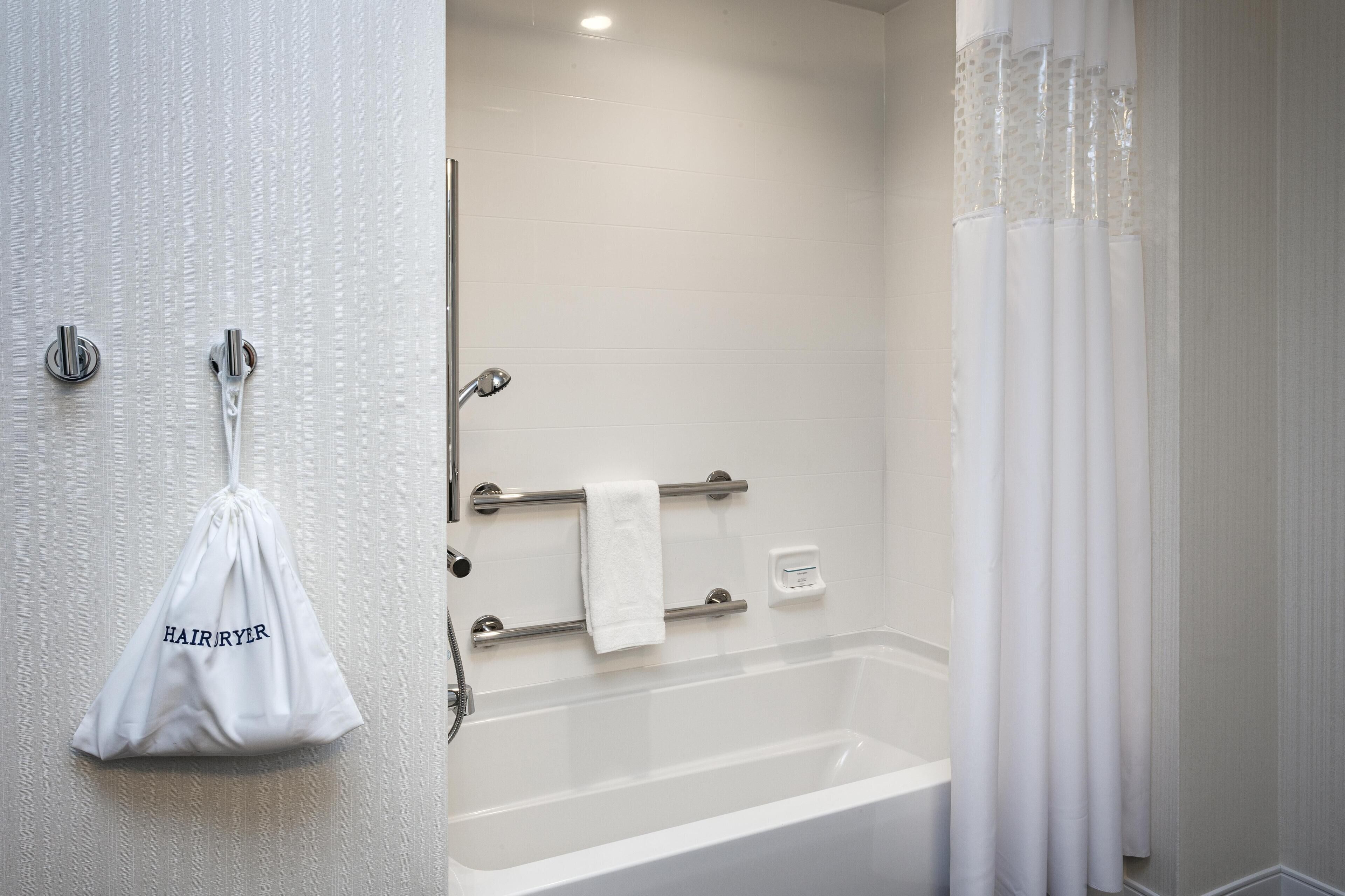 A bathroom with a bathtub, a towel rack, a hairdryer bag, and a shower curtain.