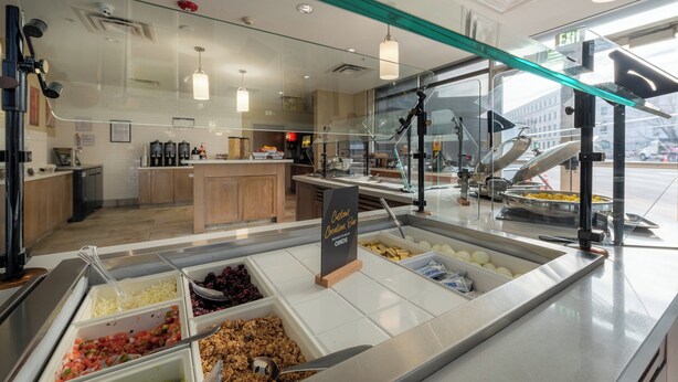 A buffet area with various food options, a sign indicating a breakfast menu, and a view of the kitchen in the background. - Staybridge Suites Denver Downtown by IHG (Denver)
