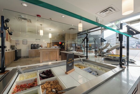 A buffet area with various food options, a sign indicating a breakfast menu, and a view of the kitchen in the background. - Staybridge Suites Denver Downtown by IHG (Denver)