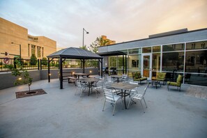 An outdoor patio area with tables and chairs, a covered seating area, and a building with large windows in the background. - Staybridge Suites Denver Downtown by IHG (Denver)