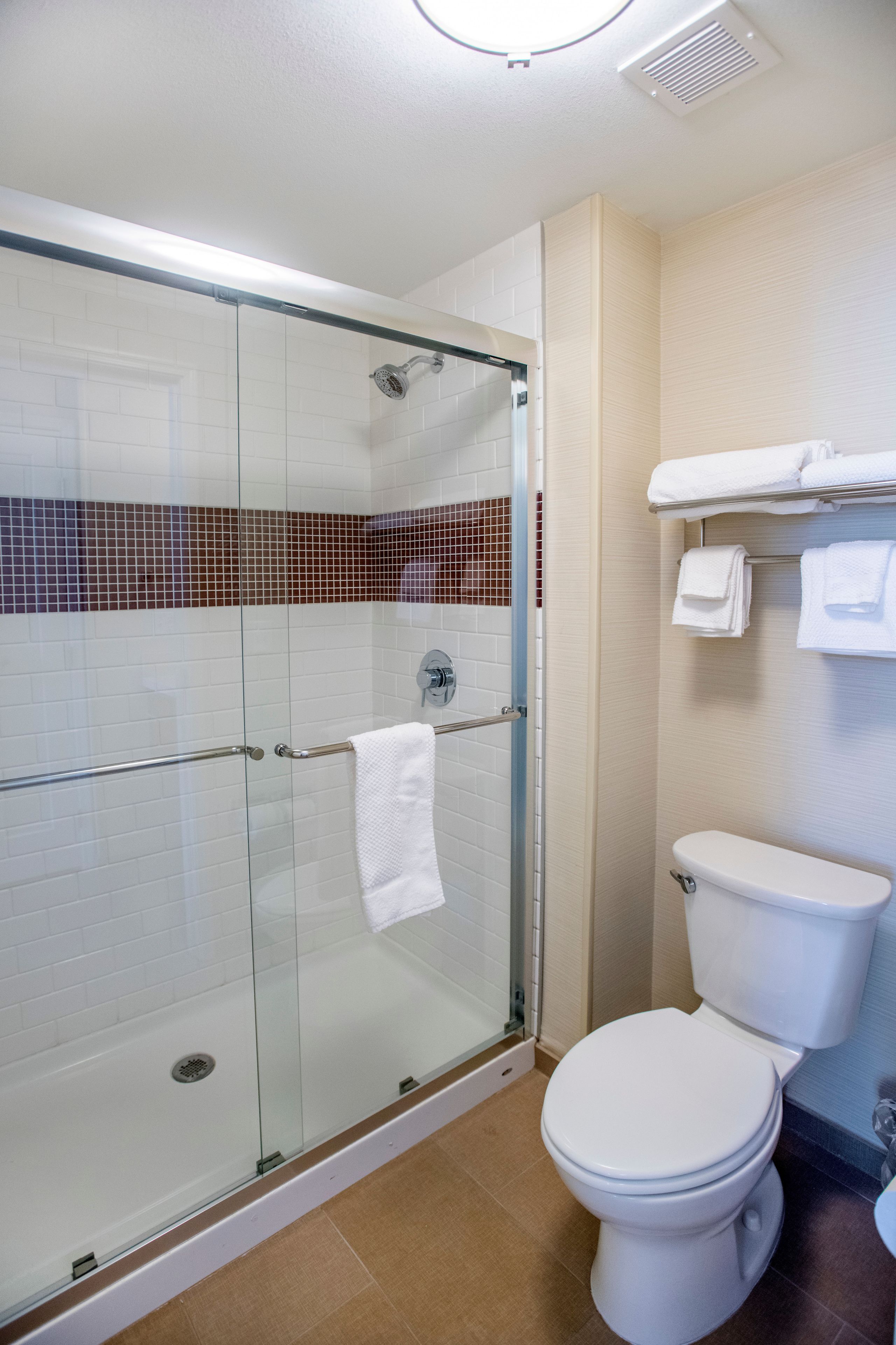 A bathroom with a glass-enclosed shower, a white toilet, and a towel rack with folded towels.