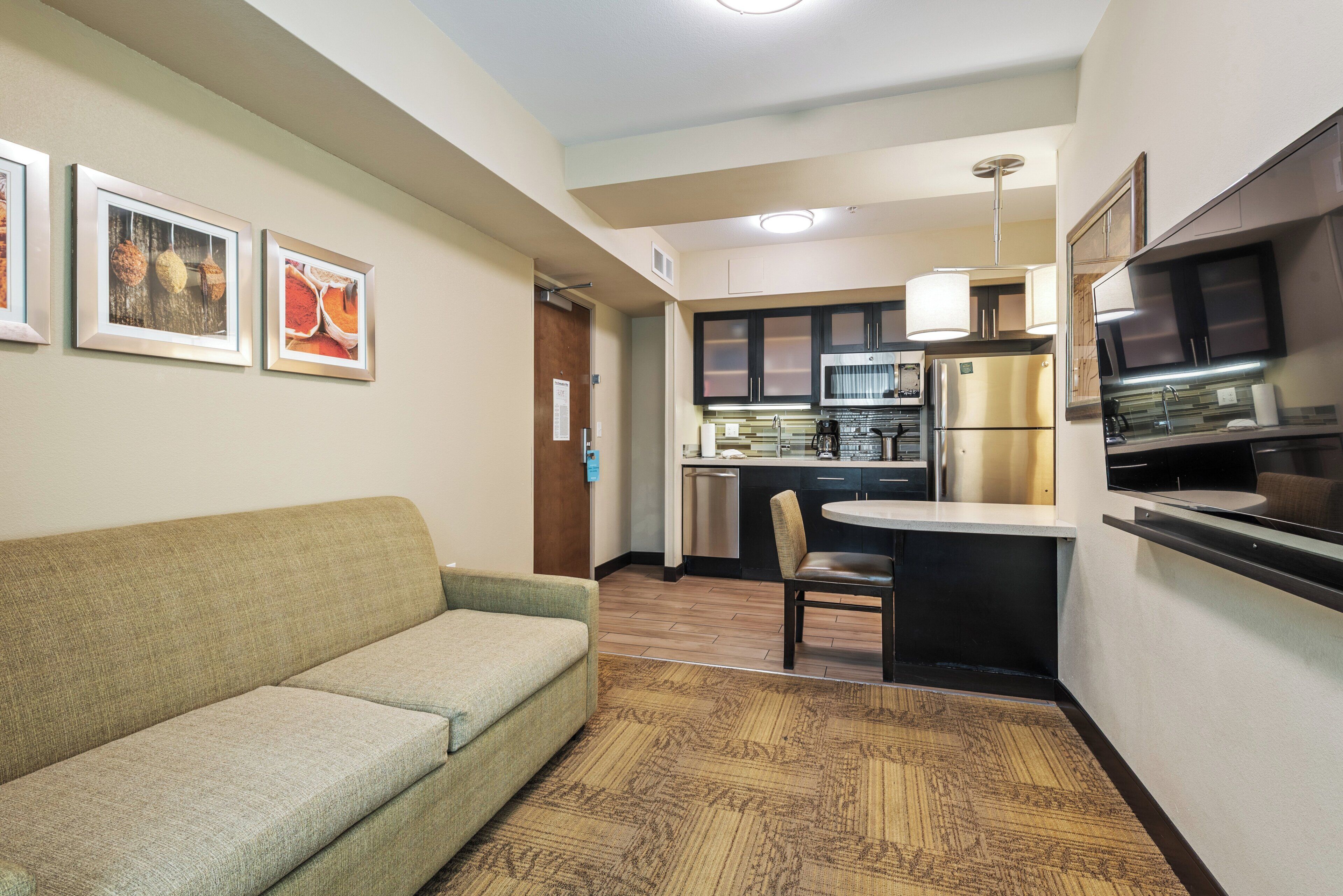 A compact kitchen with a built-in oven, a dining area with a chair, and a sofa.