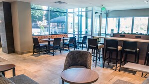 A modern lounge area with sofas, a round table, and bar stools. Large windows provide natural light and a view of the outdoors. - Staybridge Suites Denver Downtown by IHG (Denver)