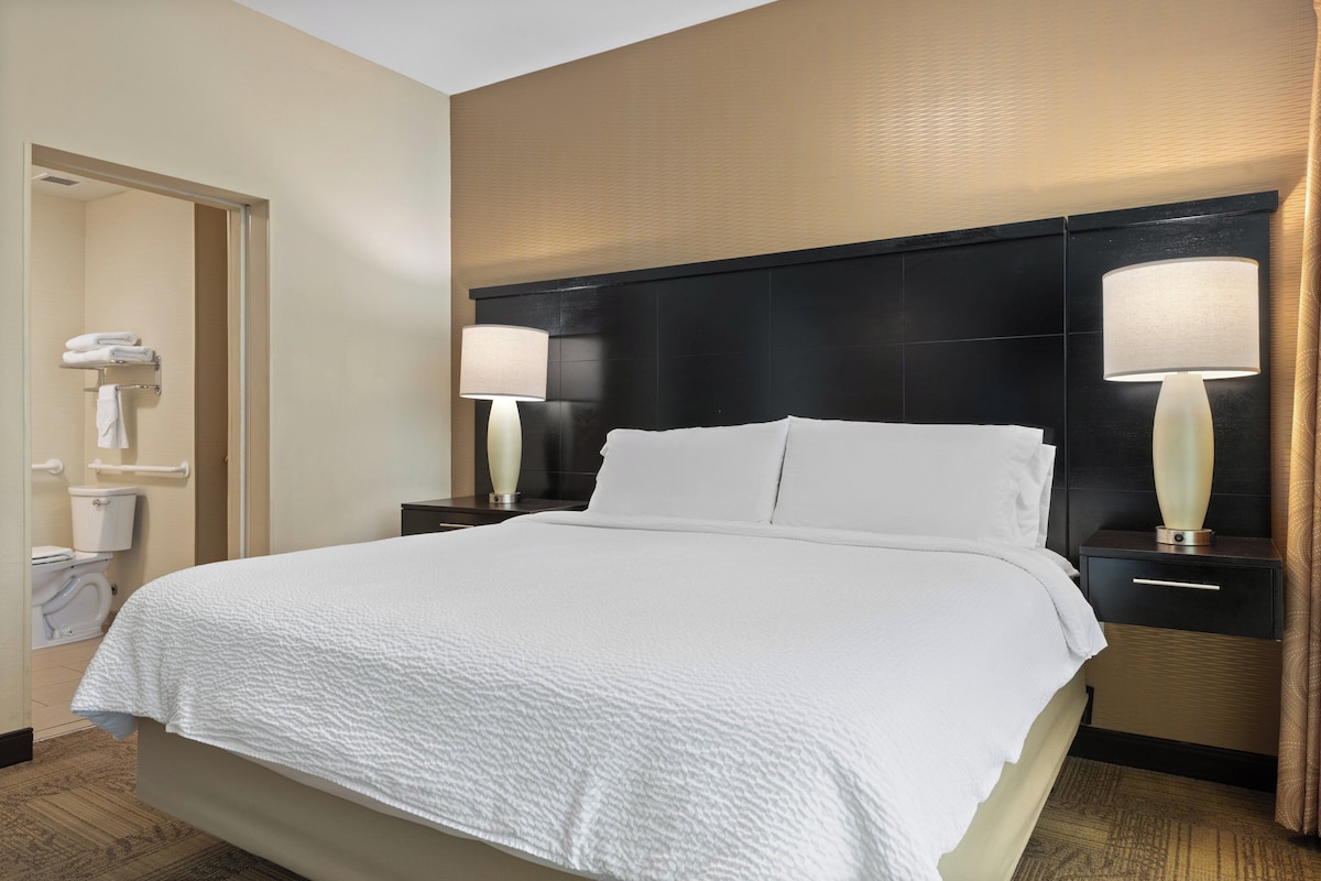 A hotel room with a large bed, two bedside tables with lamps, a bathroom with a toilet and towel rack.
