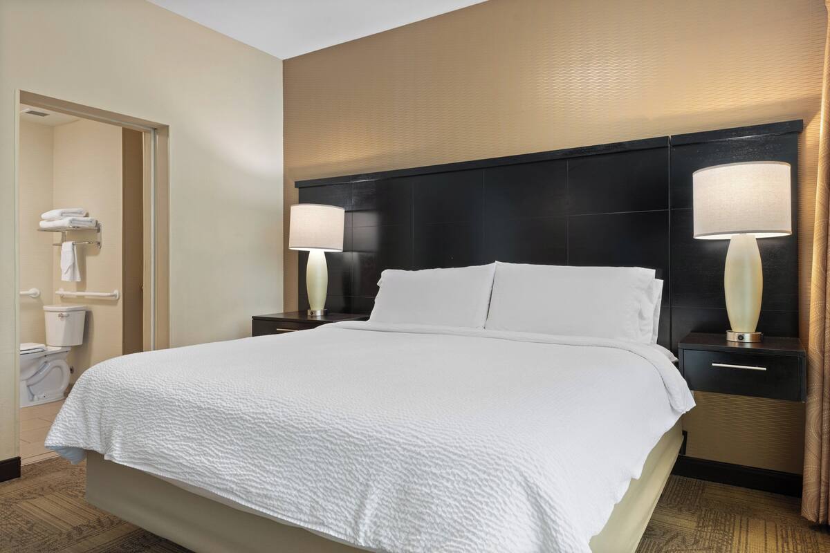 A hotel room with a large bed, two bedside tables with lamps, a bathroom with a toilet and towel rack.