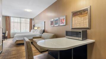 A hotel room with a bed, a sofa, a dining table, a microwave, and a large window with curtains.