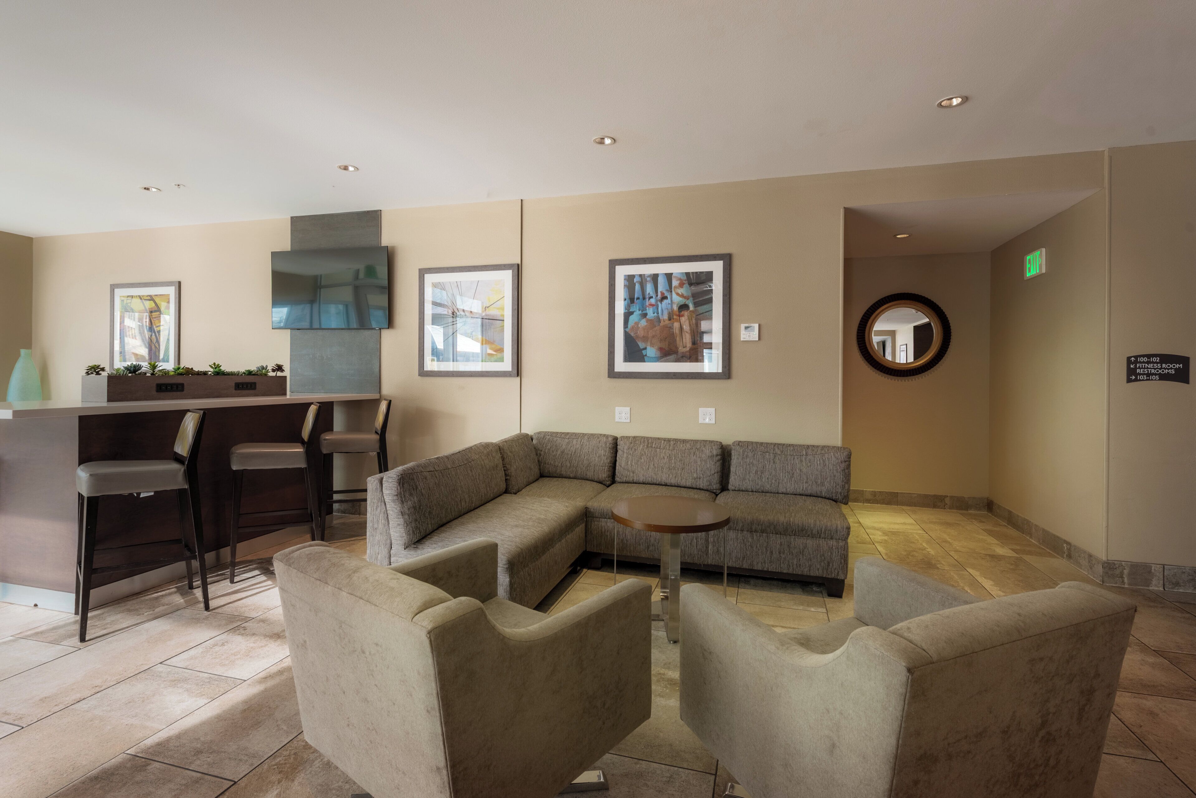 Un vestíbulo moderno con un sofá modular, una mesa redonda y una zona de bar con sillas.