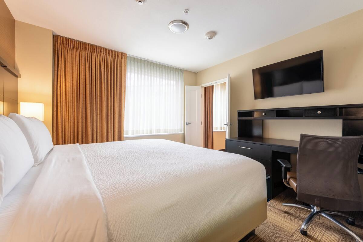 A hotel room with a large bed, a desk, a chair, a TV, and a window with curtains.