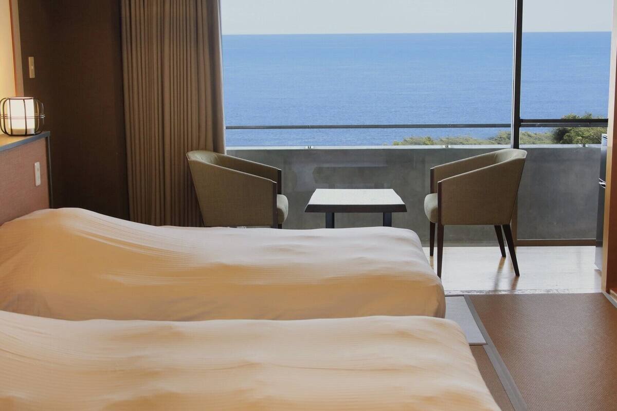 A hotel room with a bed, two chairs, a small table, and a view of the sea.