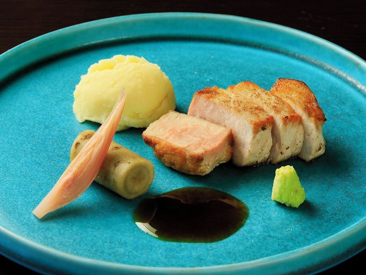 A plate with sliced meat, mashed potatoes, and a small piece of ginger.