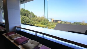 A modern hotel room with a large window offering a view of a lush green landscape and a distant building. - Soratoniwa Atami Izusan (Atami)