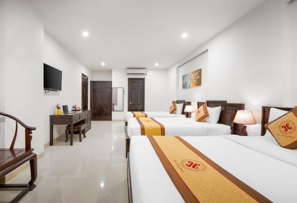 A hotel room with four beds, a desk, a TV, and a door leading to another room.