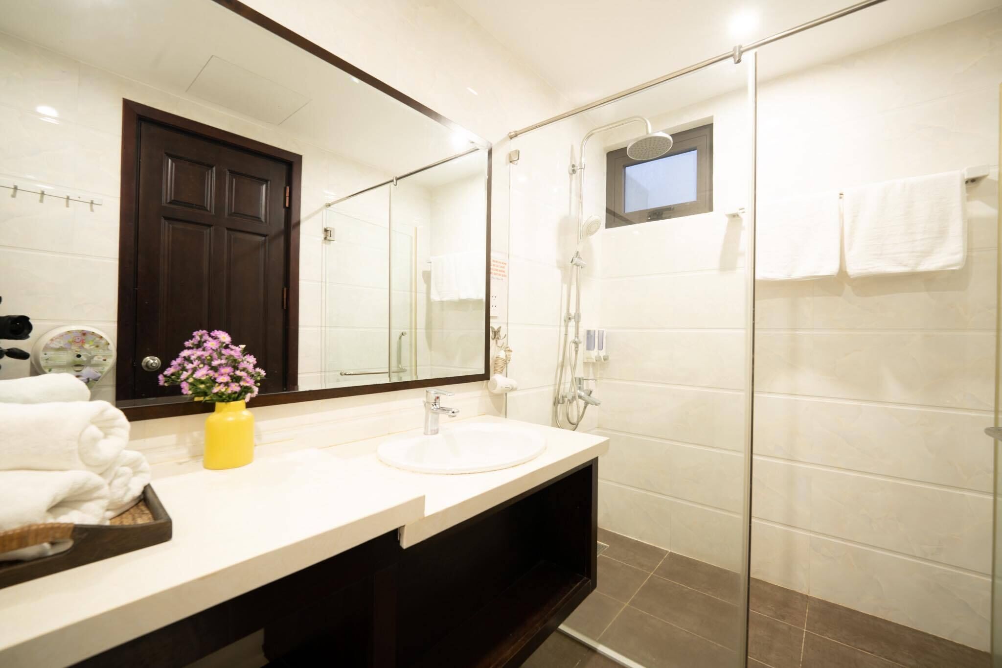 A modern bathroom with a large mirror, a sink, a shower, and a dark wooden door.