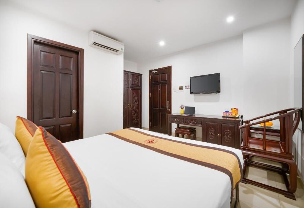 A hotel room with a bed, a desk, a chair, an air conditioning unit, and a television.