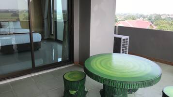 Uma varanda com porta de vidro que dá para um quarto, uma mesa verde e um banquinho pequeno.
