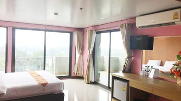Habitación de hotel con cama, escritorio, refrigerador pequeño, aire acondicionado, televisor y balcón con vistas.