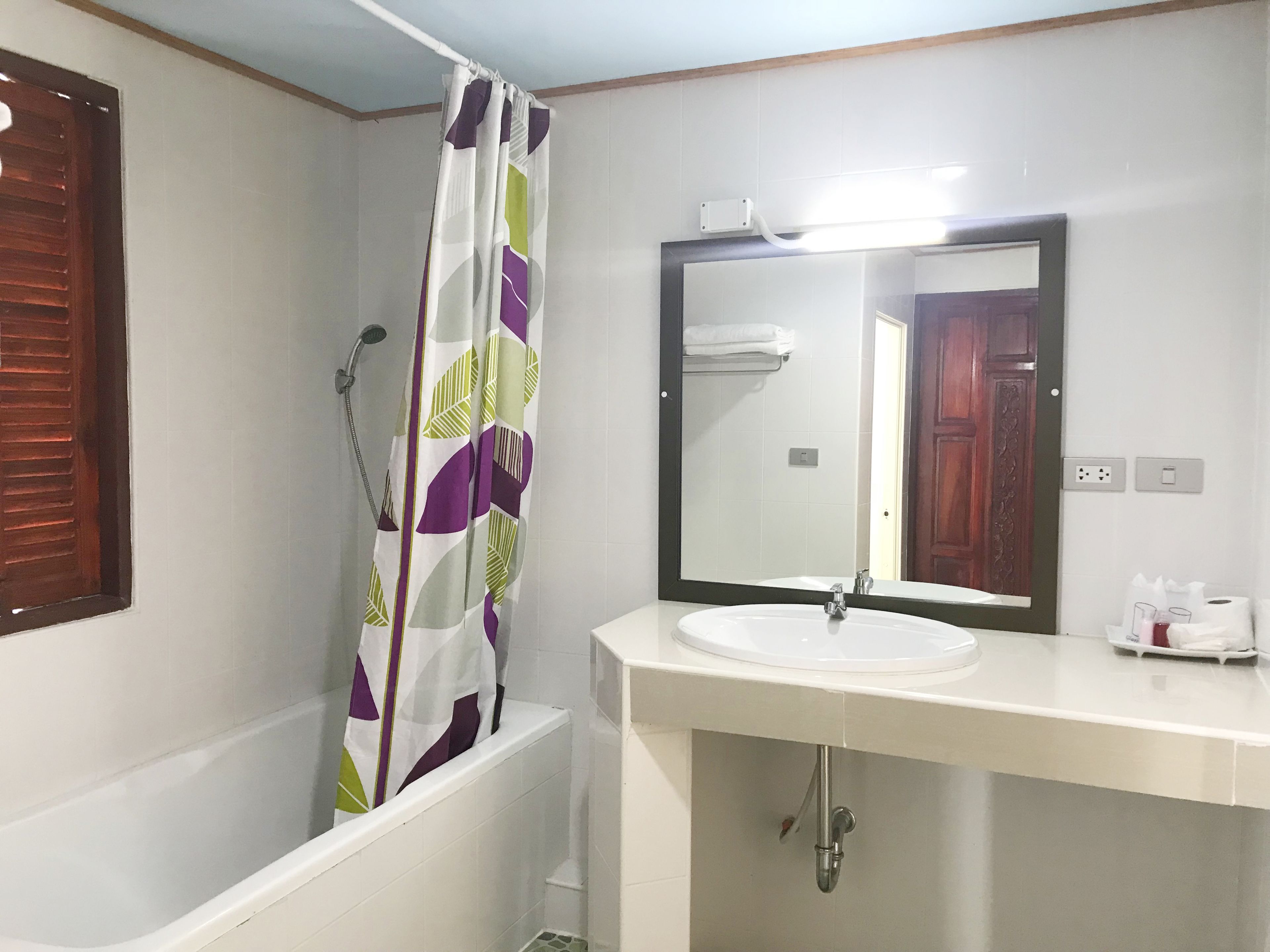 A bathroom with a bathtub, a shower curtain, a sink, and a mirror.