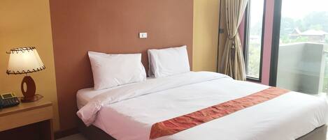Habitación de hotel con una cama grande, una lámpara de noche, un teléfono y una ventana con cortinas.