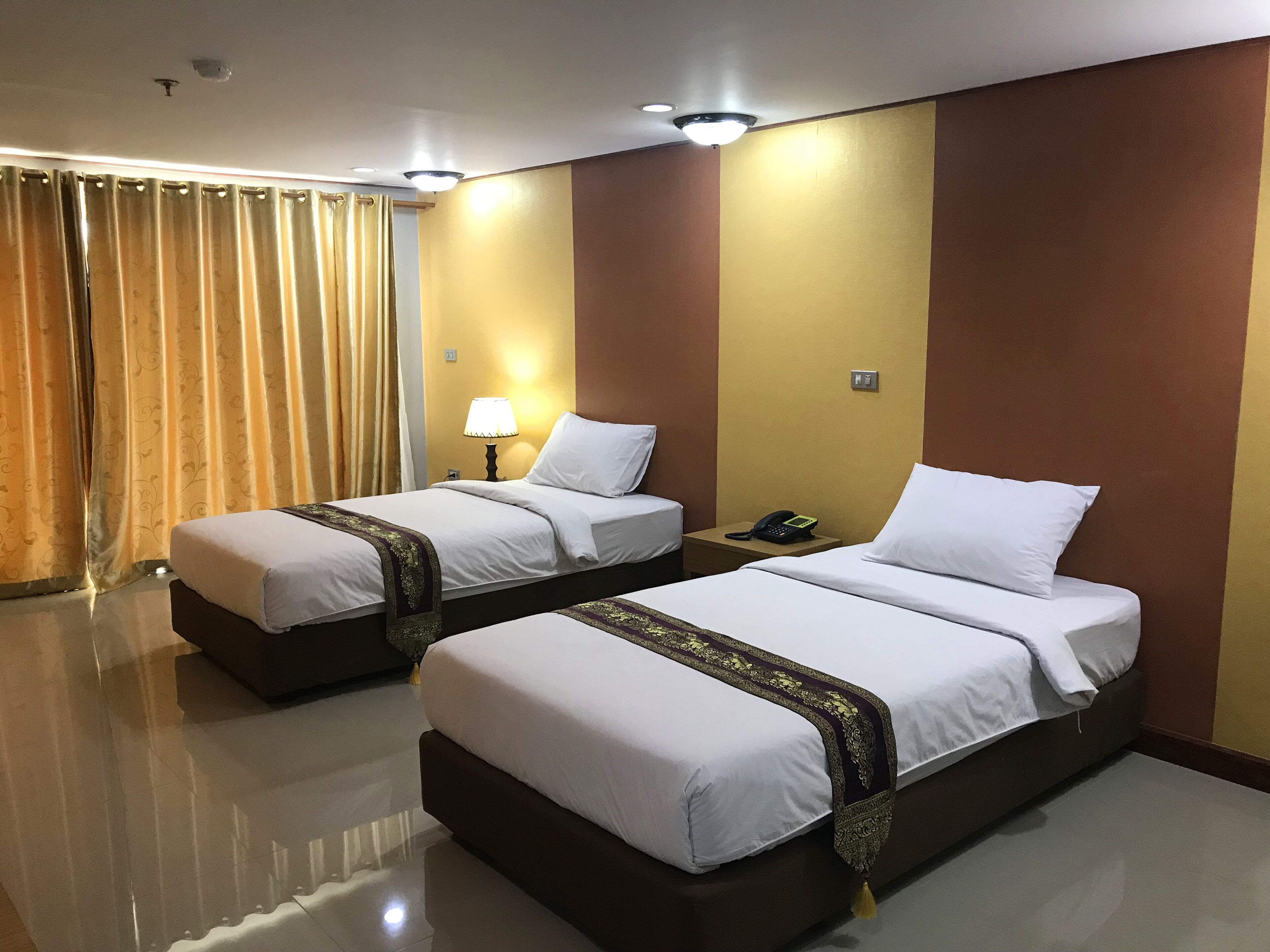 Quarto de hotel com duas camas, mesa de cabeceira com telefone, luminária e cortina.