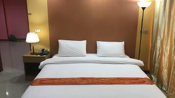 A hotel room with a bed, two pillows, a nightstand with a lamp, and a curtain.