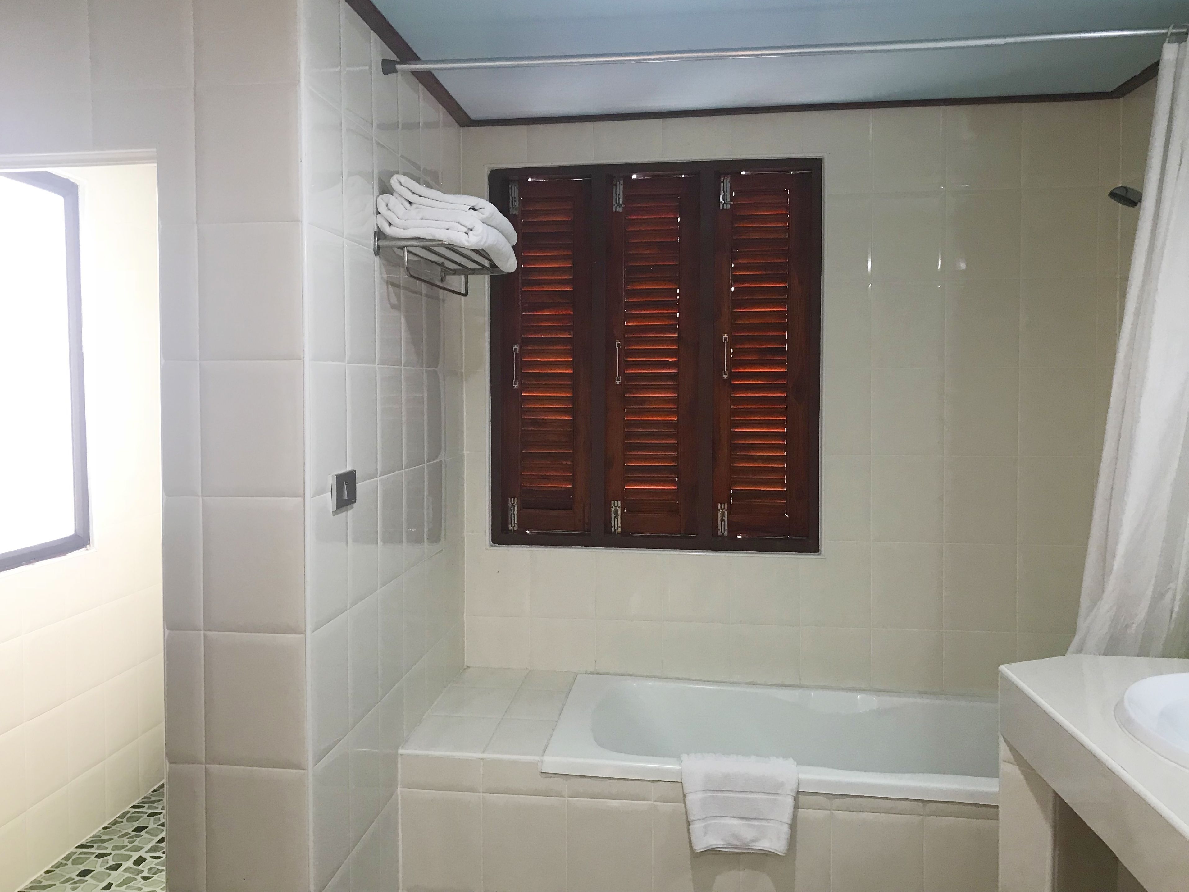 Um banheiro com banheira, porta-toalhas com toalhas, janela com persianas de madeira e cortina de chuveiro.