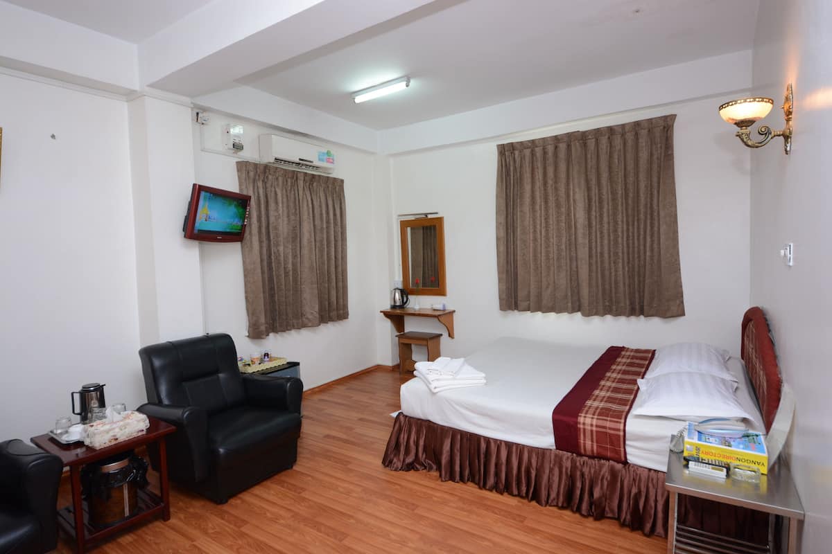 Habitación de hotel con cama, una silla, una mesita con hervidor, televisión y espejo.