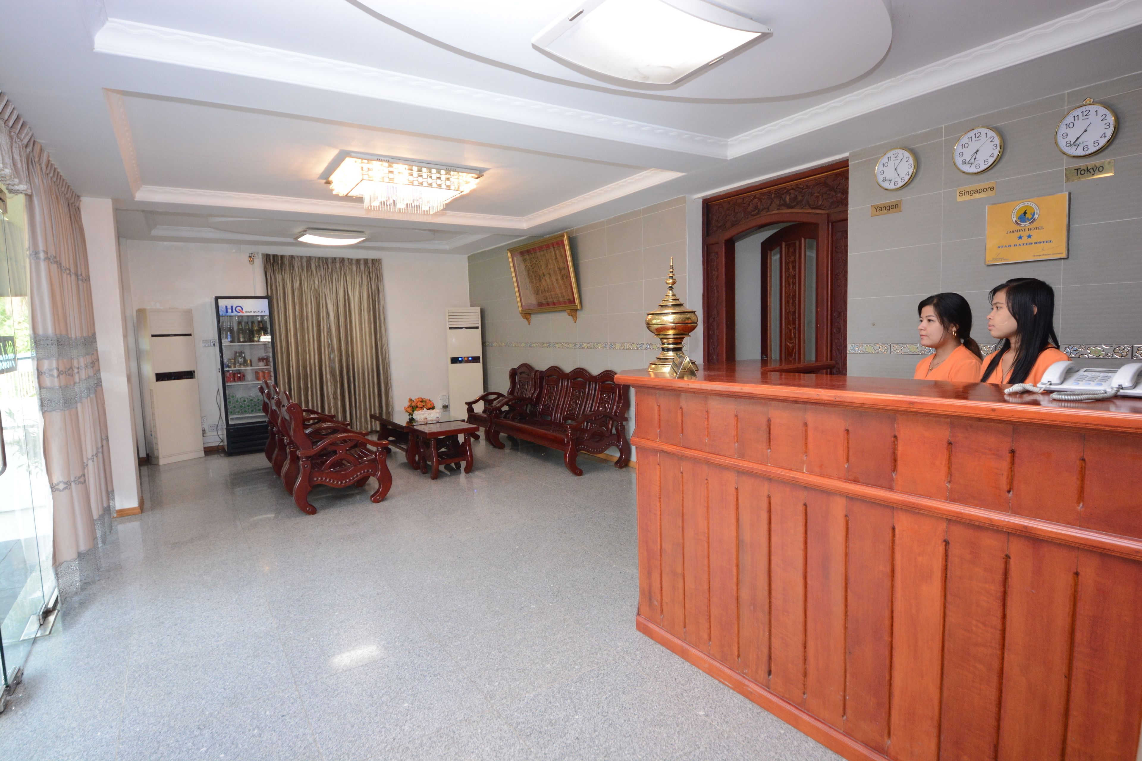 A hotel reception area with a wooden reception desk, a chandelier, a clock, and a sign indicating the hotel is in Singapore.