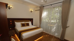 Une chambre d’hôtel avec un grand lit, une tête de lit en bois, des tables de chevet et une vue à travers des rideaux transparents.