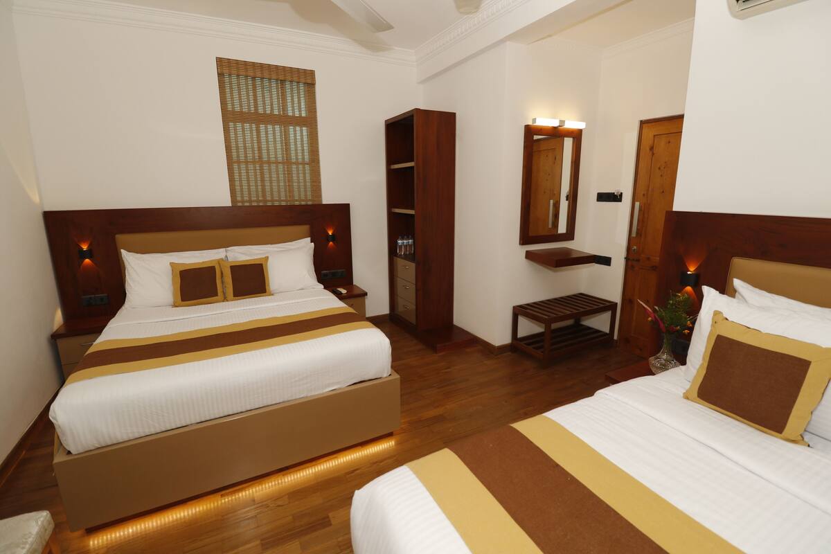 A hotel room with two beds, wooden headboards, a small table, a mirror, and a wardrobe.