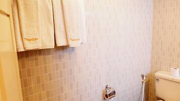 A bathroom with a toilet, a paper towel dispenser, and three towels hanging on a rack.