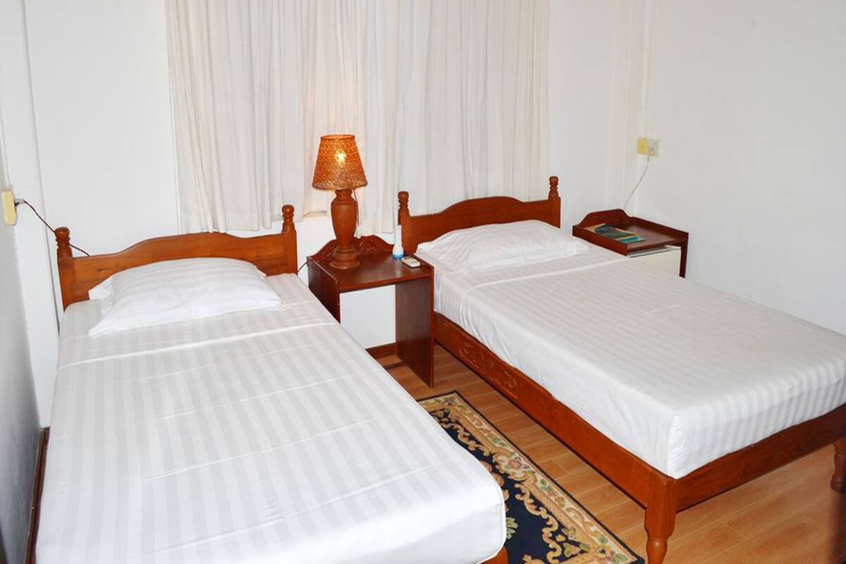 A double room with two single beds, a bedside table with a lamp, a nightstand, and a small bedside table with a book and a phone.