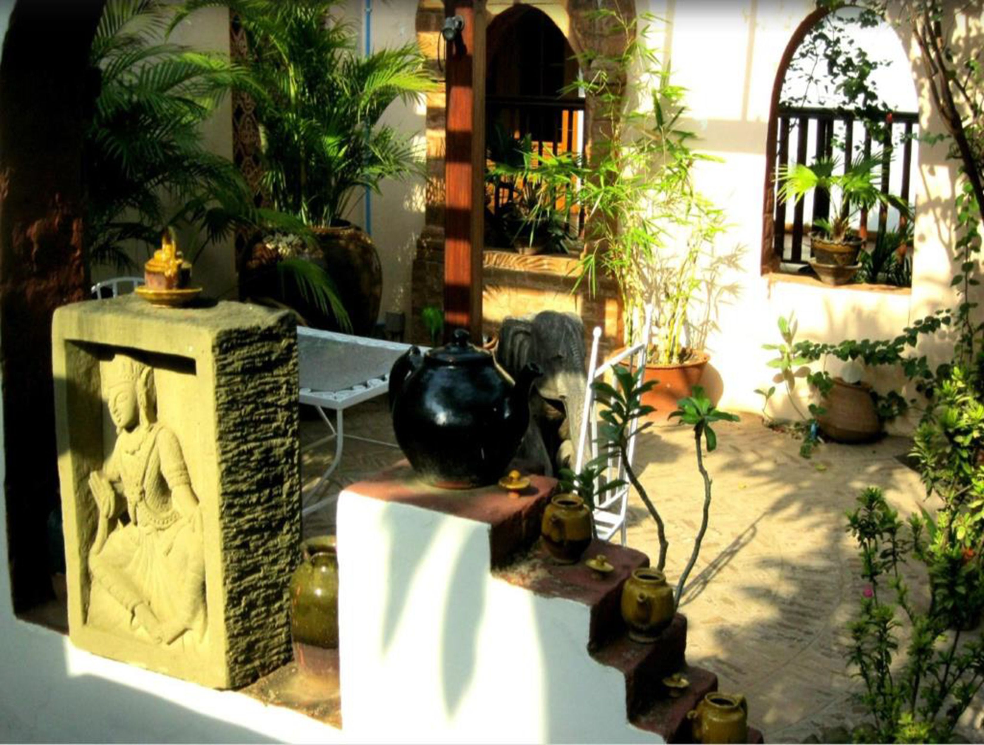 Un patio con una escultura de piedra, una maceta negra y varias plantas en macetas.